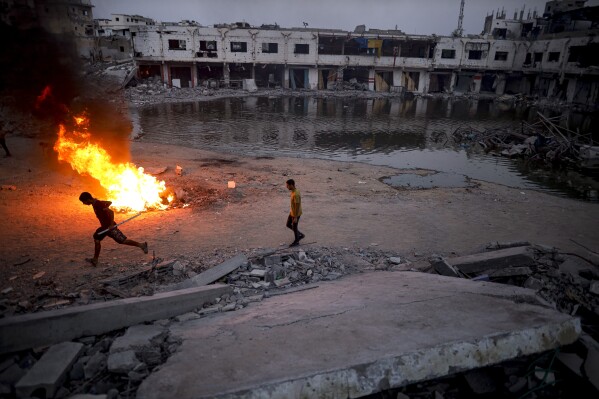 Palestinians displaced by the Israeli air and ground offensive on the Gaza Strip, light a fire to keep away mosquitoes and other insects, which have recently infested the streets of the southern town of Khan Younis, Gaza Strip, Thursday, July 4, 2024. (AP Photo/Jehad Alshrafi)